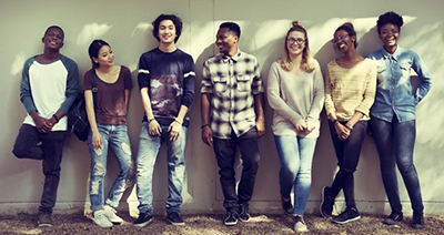 Diverse group of teens standing outside leaning against a wall