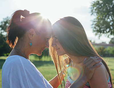 Mother and teen daughter hugging outside with foreheads touching