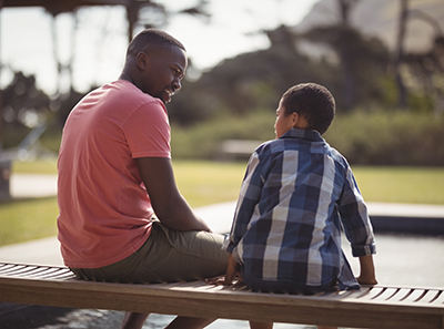 Man and son sitting on bench outside having pleasant conversation