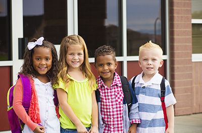 Diverse group of happy elementary age children standing outside school